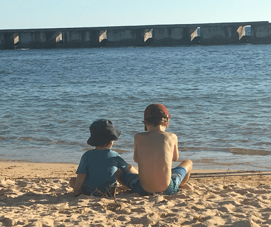 Lukas and Sawyer sitting on the beach with the concrete break water wall in the background. Playa Girōn a spot not to be missed.