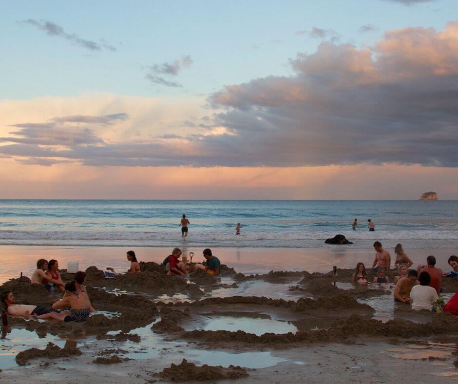 Hot Water Beach at sunset as tourists and local relax in their sandy spa pools