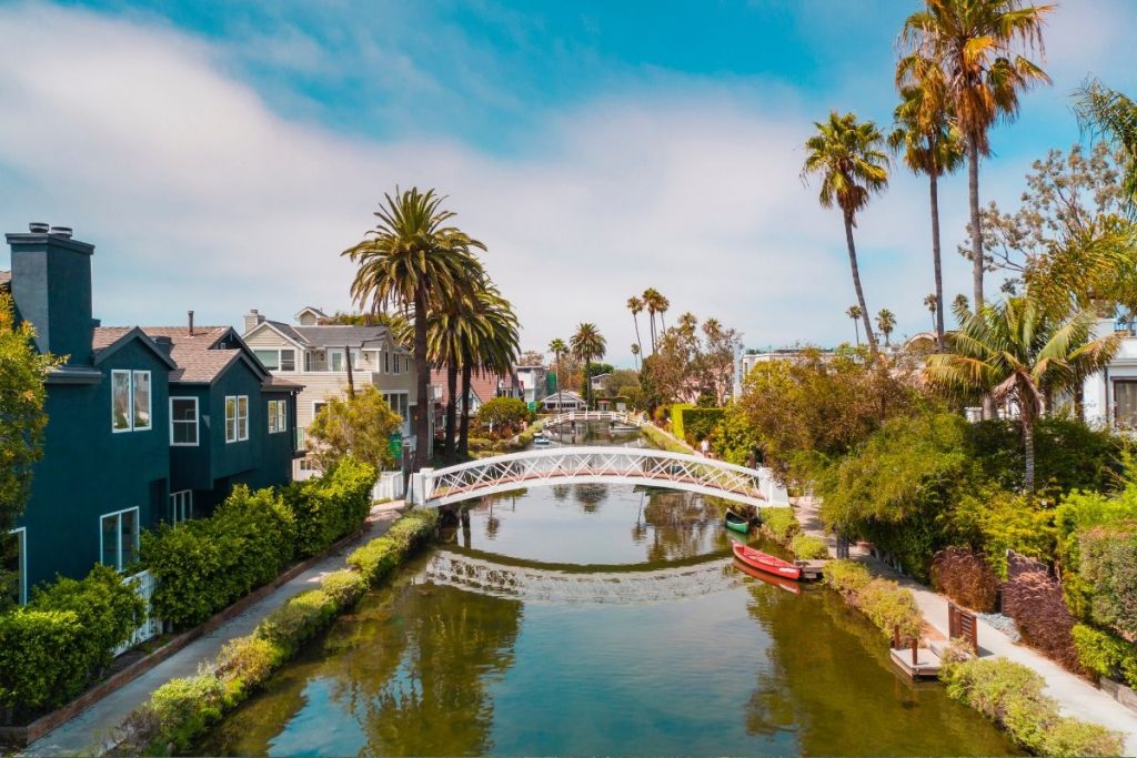 looking down the Venice Canal on a calm day, houses line either side with a white bridge connecting both sides