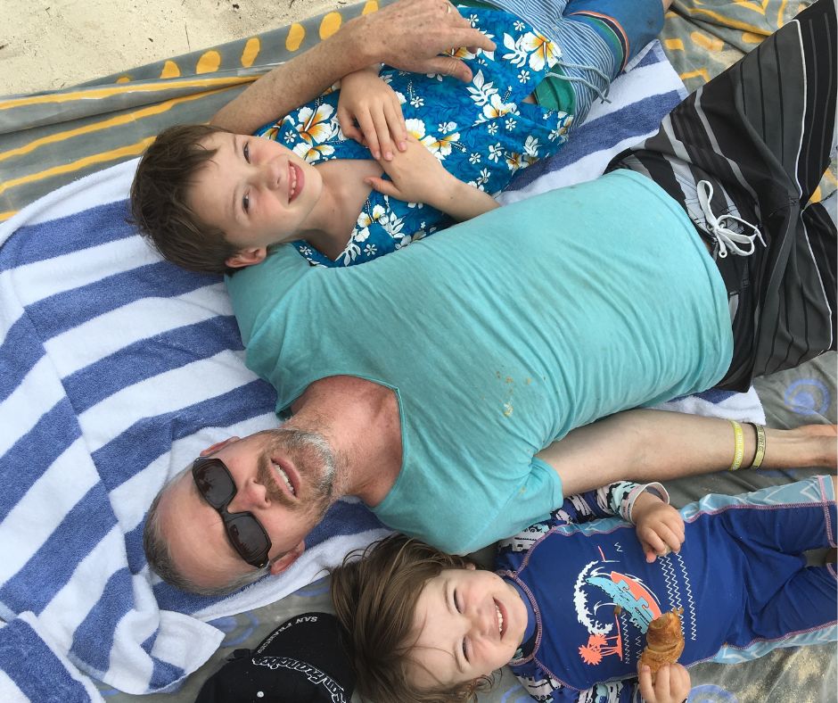 The boys laying on the beach towels looking up at the camera