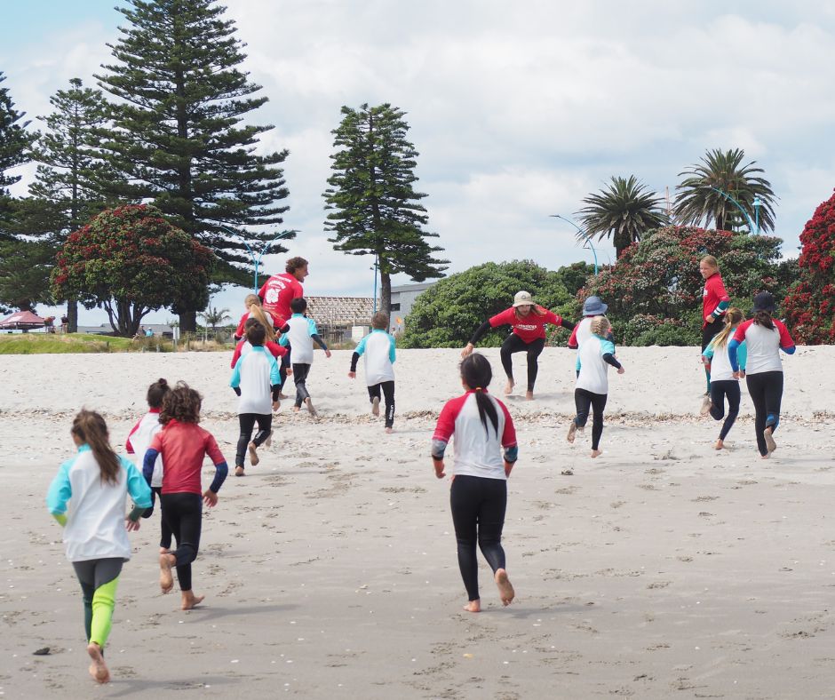 A group of kids running up the beach towards their instructors making it one of the best Mount Maunganui Surf Lessons