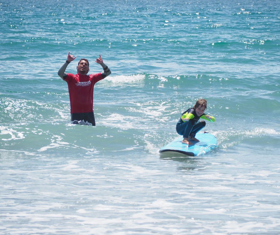 Small child catching a wave with the instructor doing a shaka