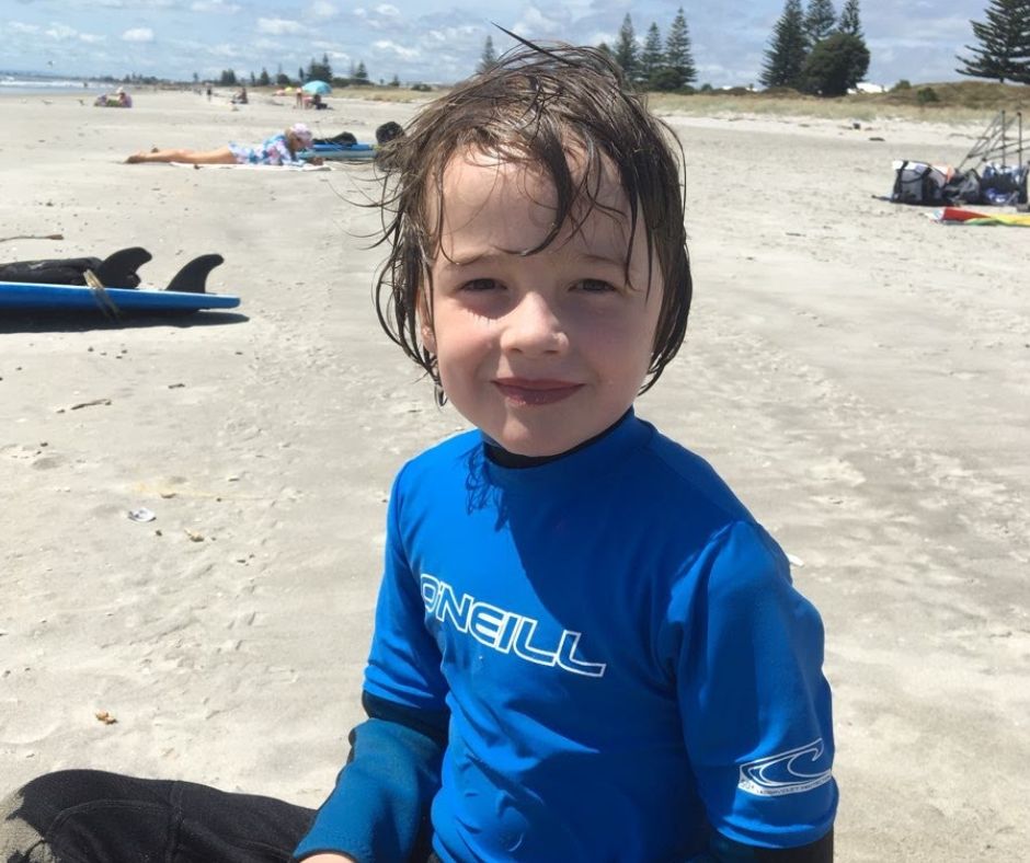 Lukas sitting on the beach from one of his Mount Maunganui surf lessons