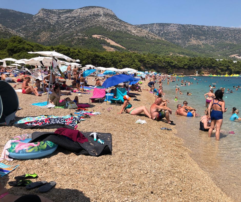Looking along Zlatni Rat beach, with people relaxing in the waters and the mountains in the background
