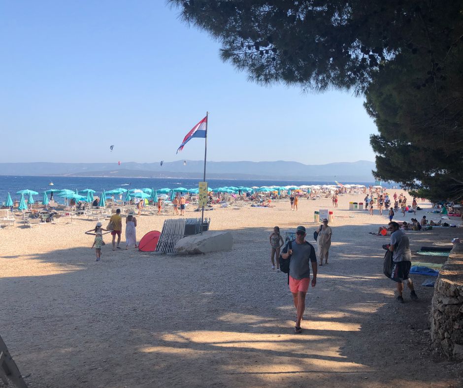 Our first steps onto Zlatni Rat beach, with the Croatia flag and shore lined umbrellas