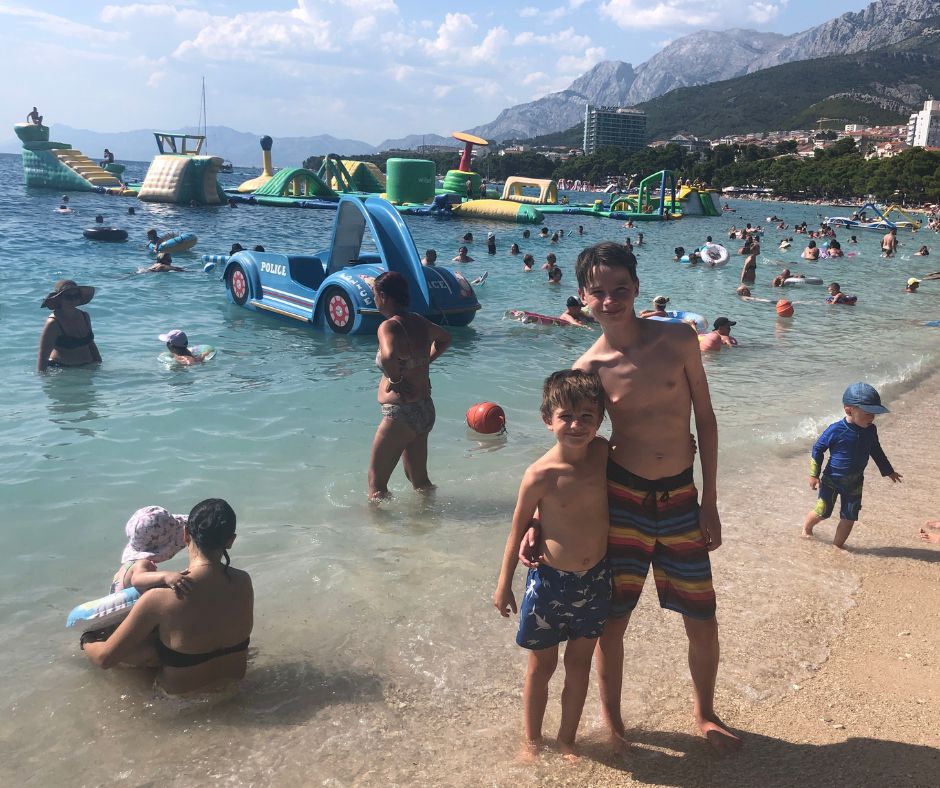 The boys posing on Makarska beach with the crowds and aqua park in the background