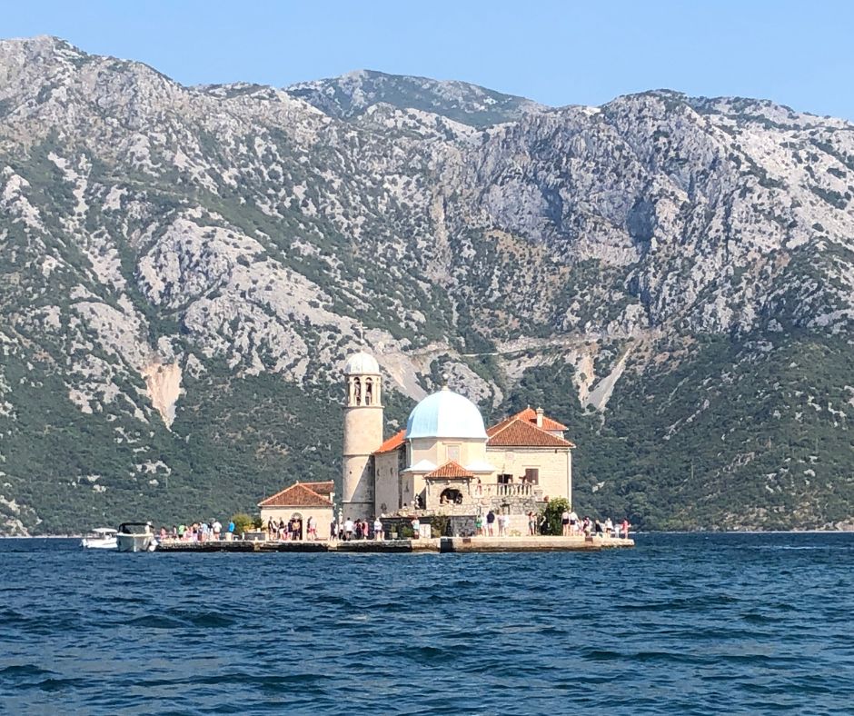 The Church of Our Lady of Škrpjela from the boat with the mountains in the background