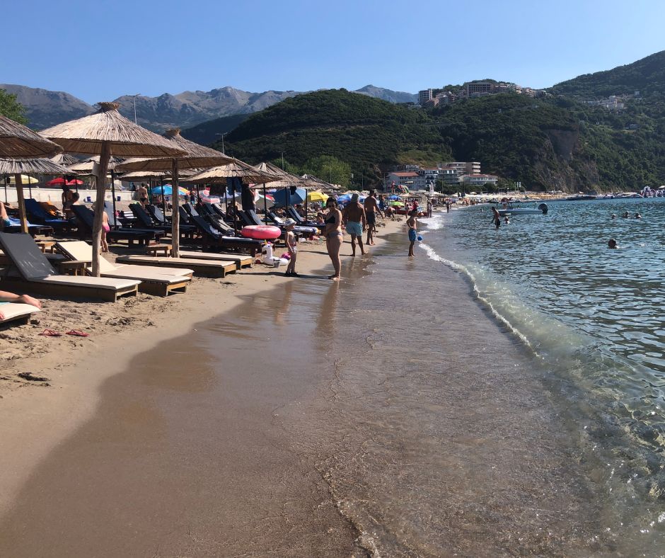 Looking down the shoreline are all the sun loungers, prople standing around and people swimming