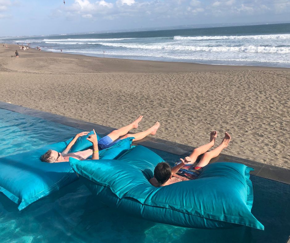 Dad and Lukas on the inflatable pillows on the edge of the pool looking across the beach at the waves